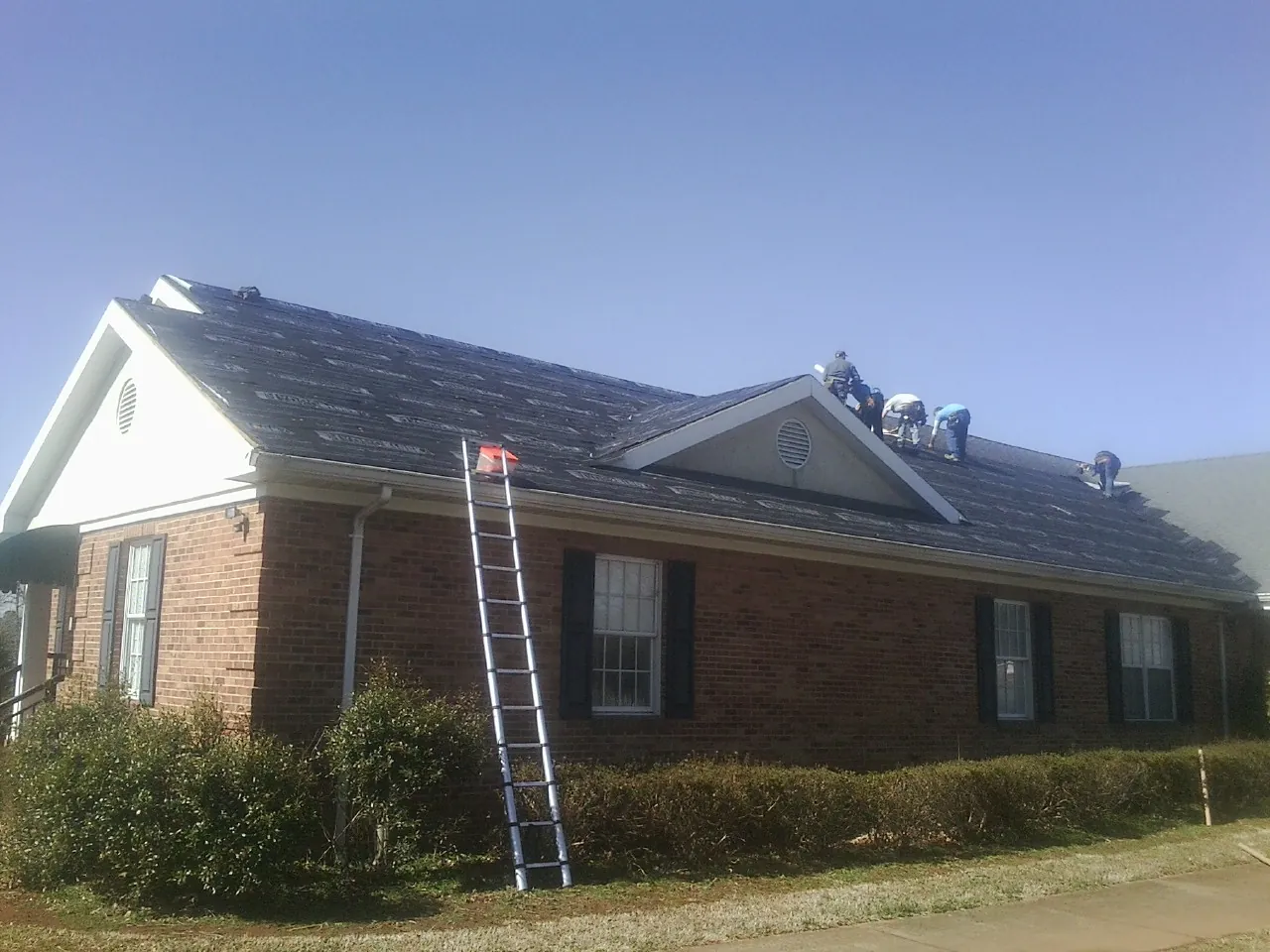 Crew tearing shingles off a brick ranch roof with a ladder set — Emergency Roof Repair work by our crew in Epping