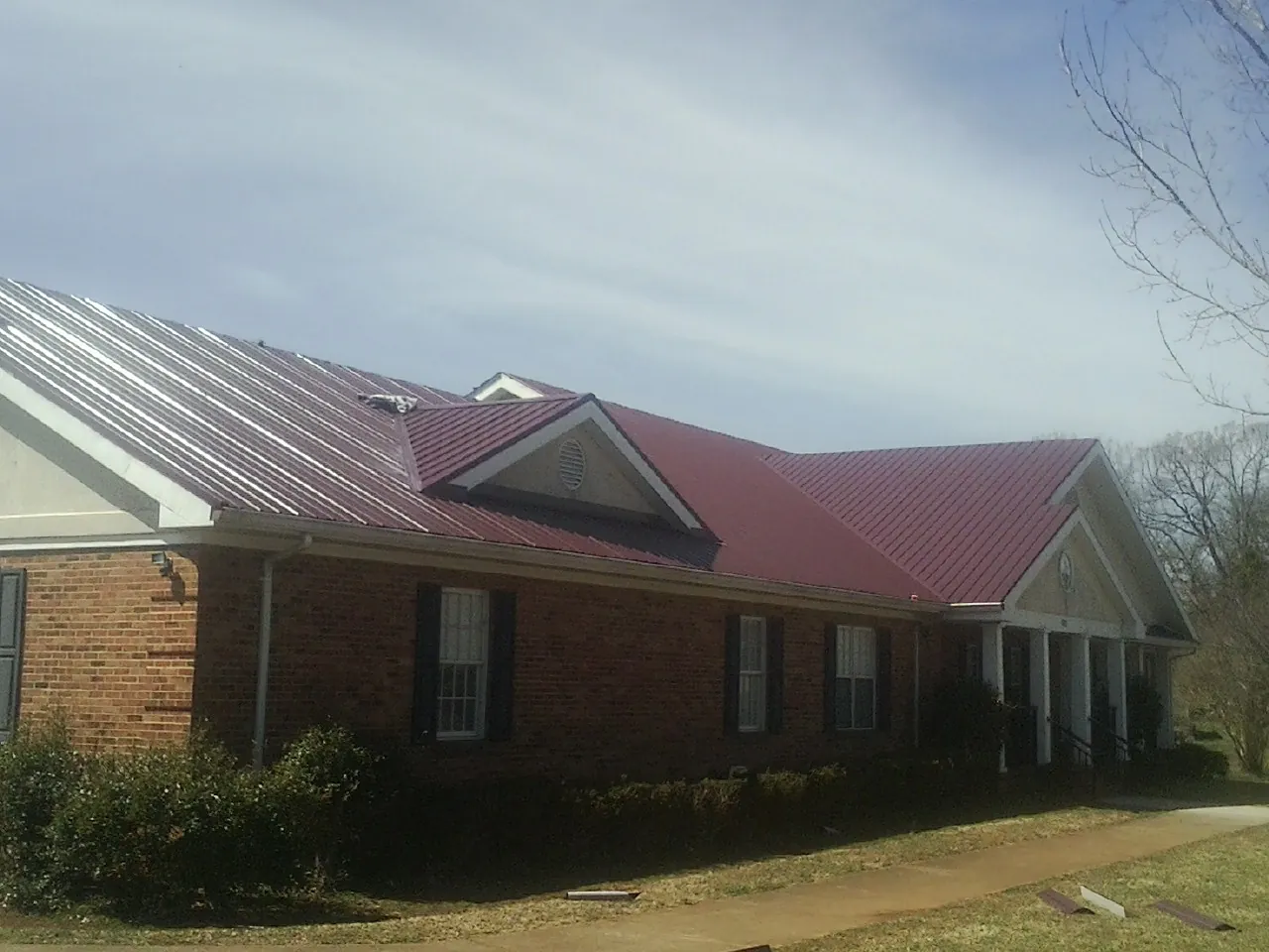 Red metal roof with gabled entries on a long brick building, from a Hail Damage Roof Repair job in Epping