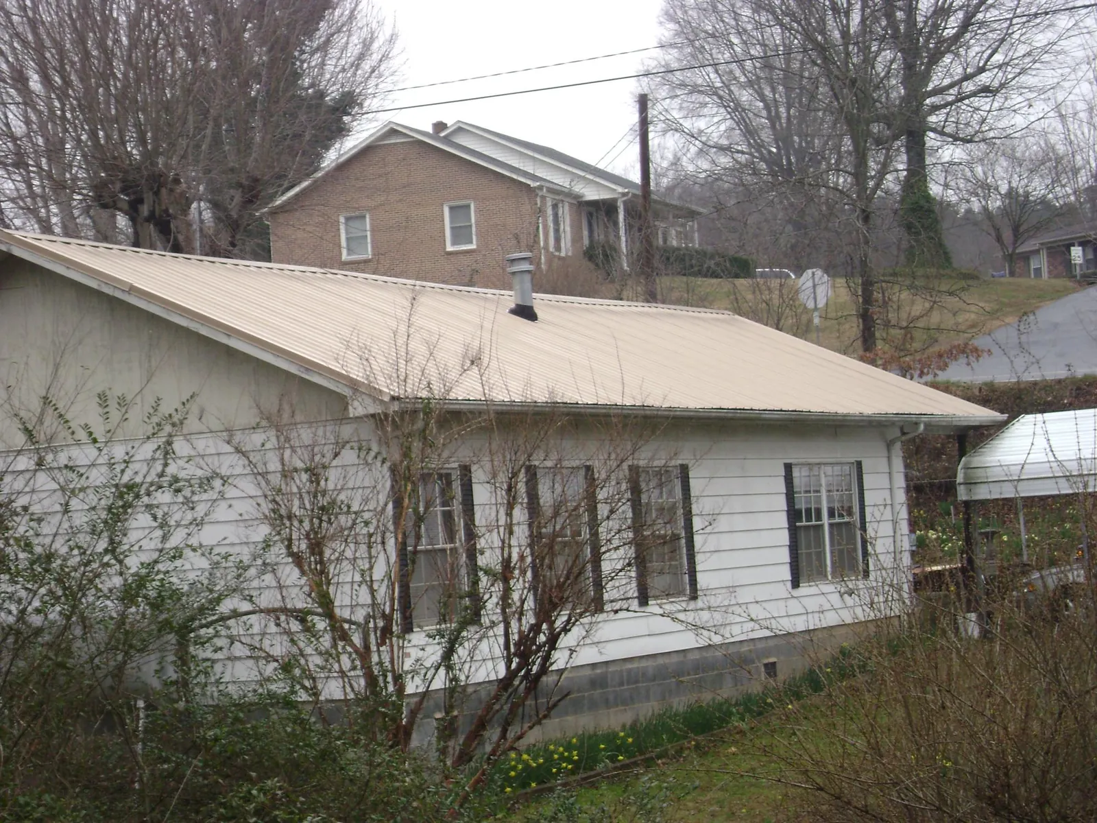 Tan metal roof on a white sided house set into a hillside — Commercial Roofing by Roofing Brothers in Epping