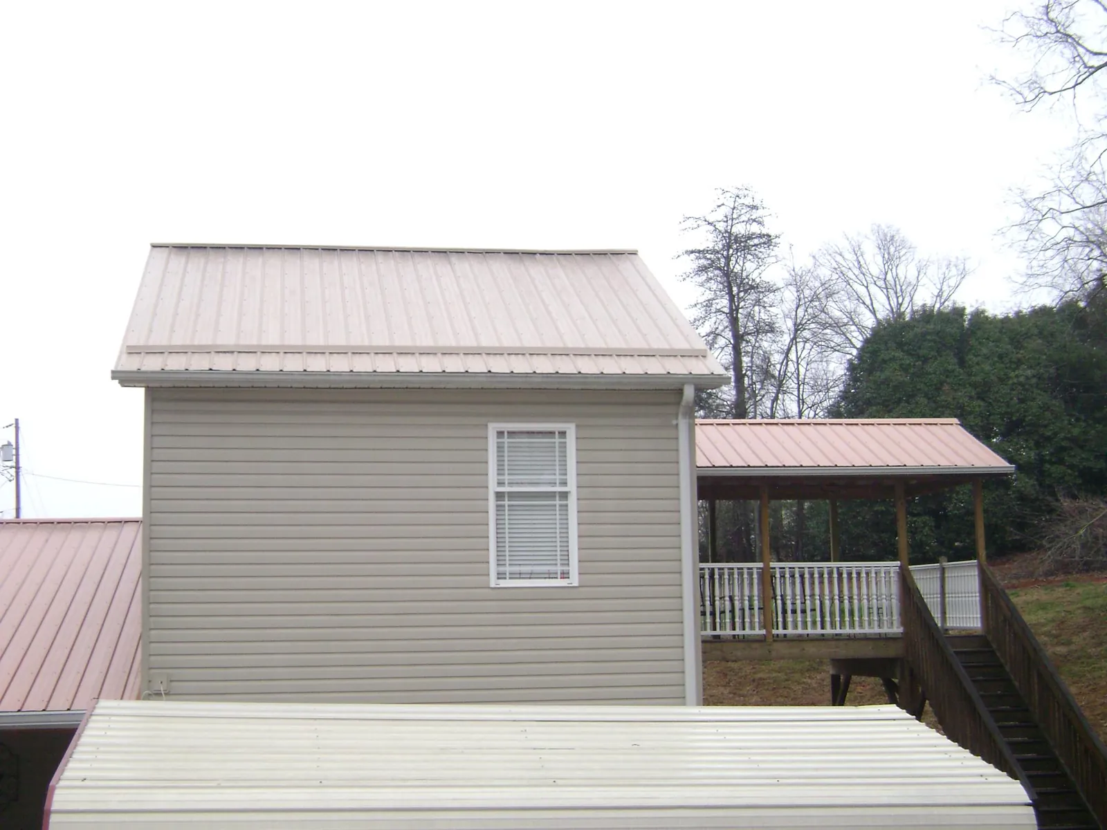 Tan metal roofs on a two story addition and attached porch, from a Roof Replacement job in Epping